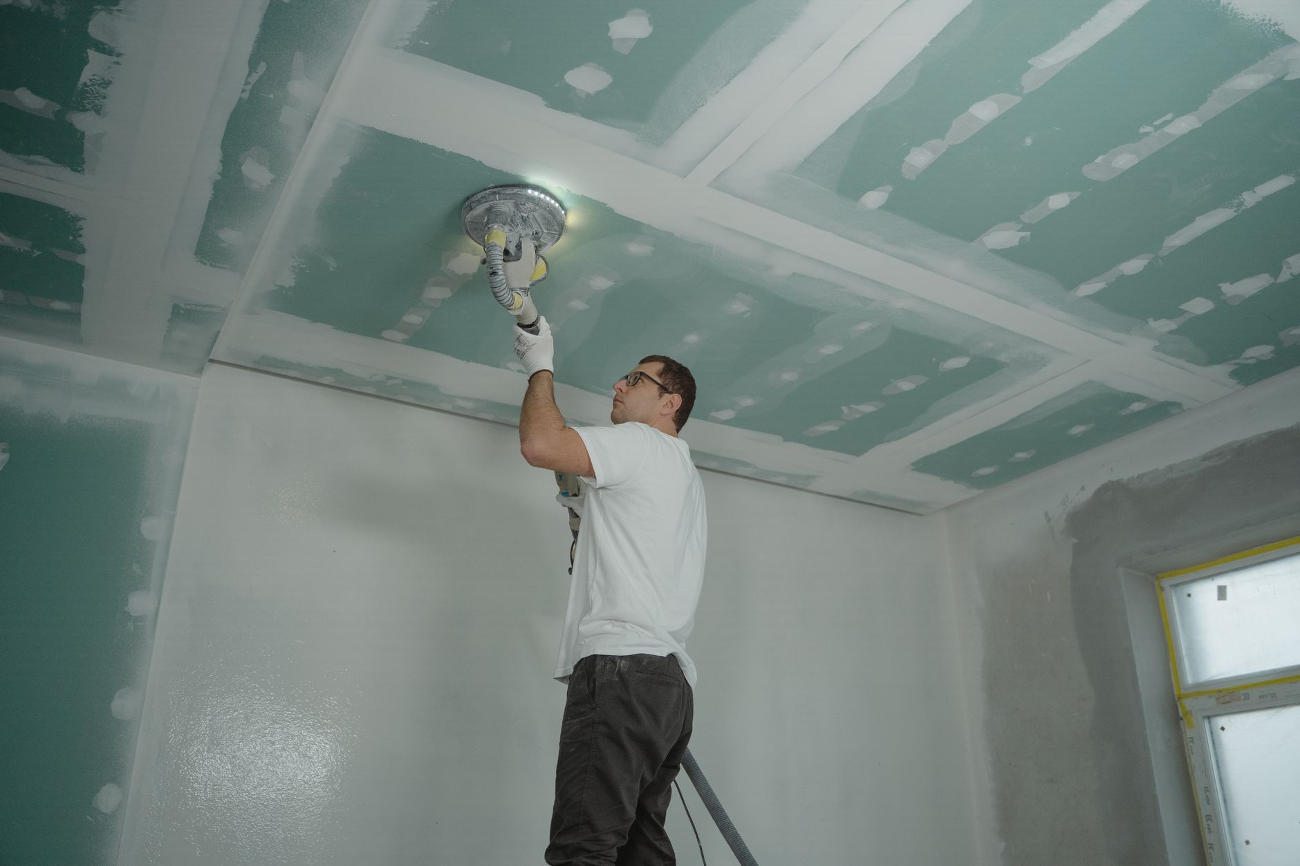 Vakman schuurt een net gevoegd gipsplaatplafond met een langnekschuurmachine