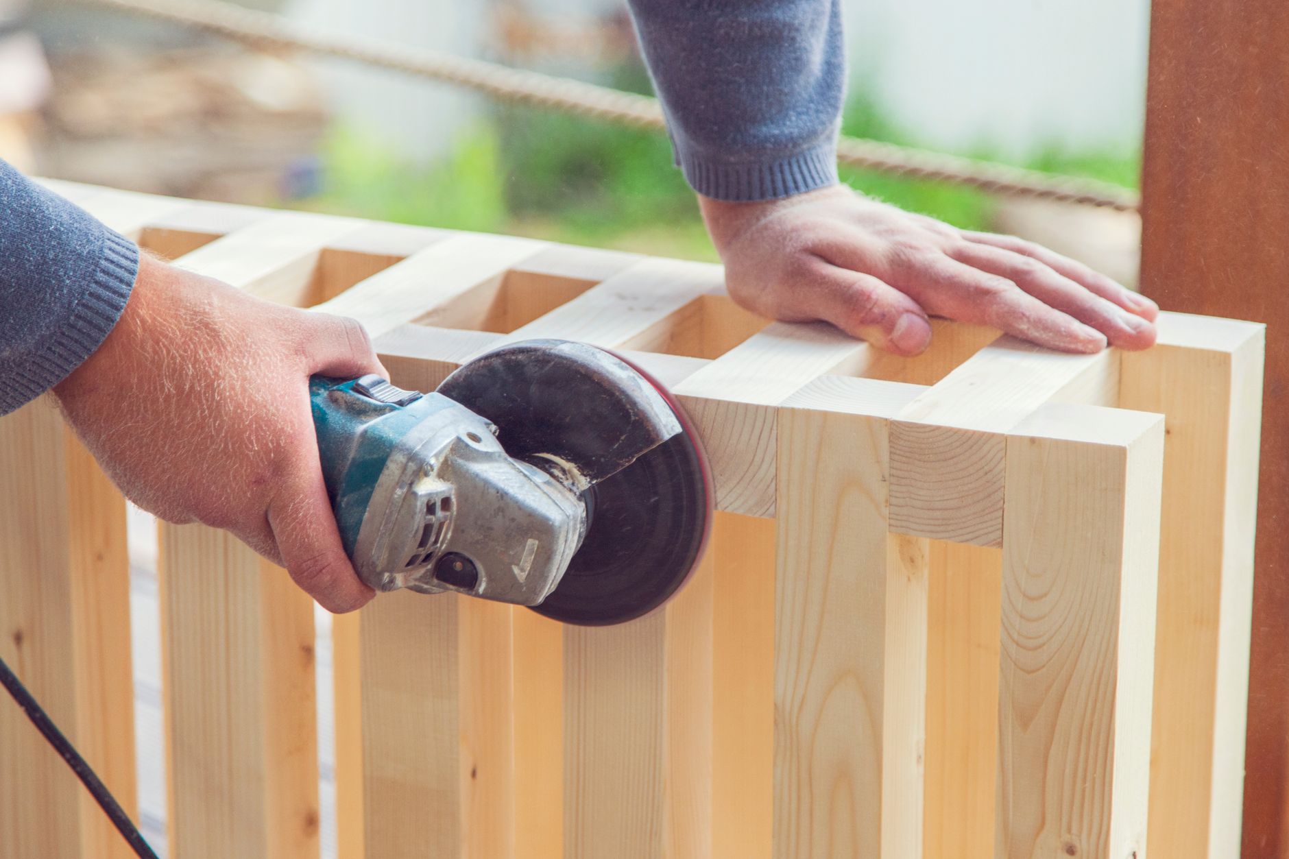 Vakman schuurt een houten lattenconstructie glad met een schuurmachine