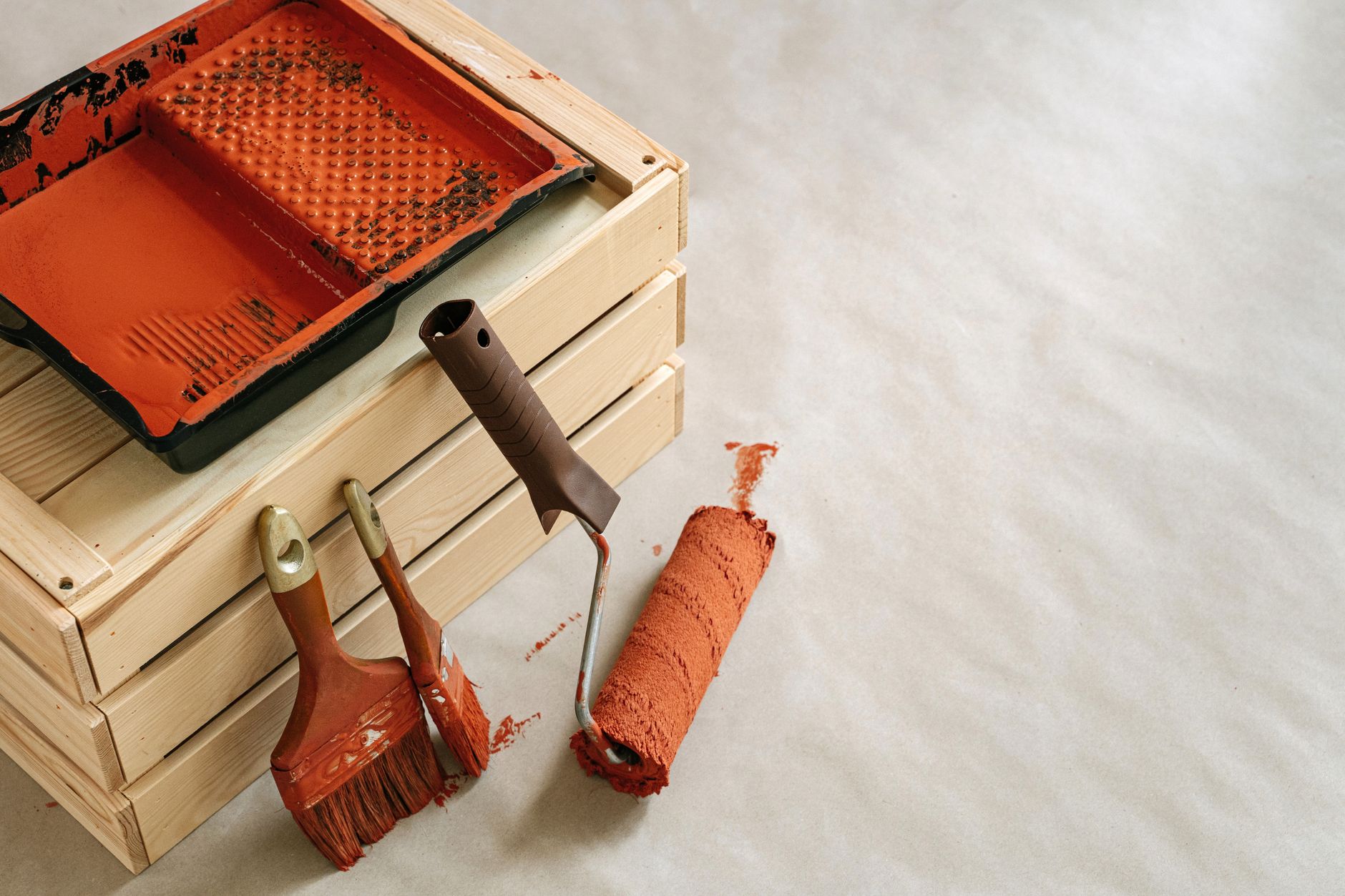 Verfbak, roller en kwasten met terracotta verf op een houten kist